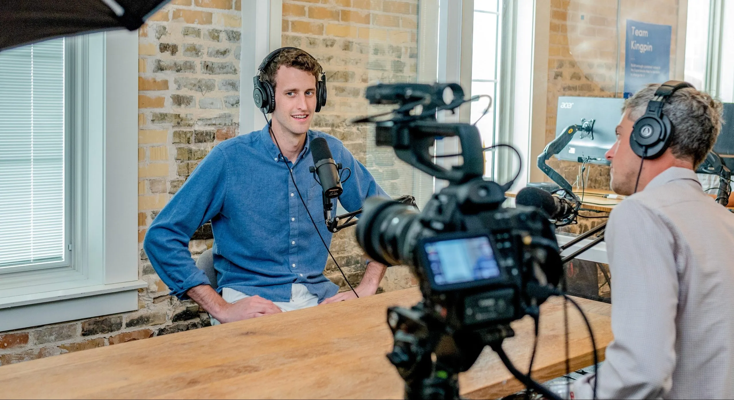 Two men speaking into microphones while recording a podcast in front of a camera