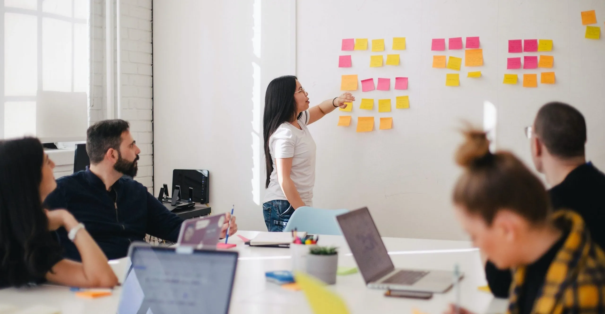 Woman presenting numerous post-it notes on a whiteboard at a team meeting