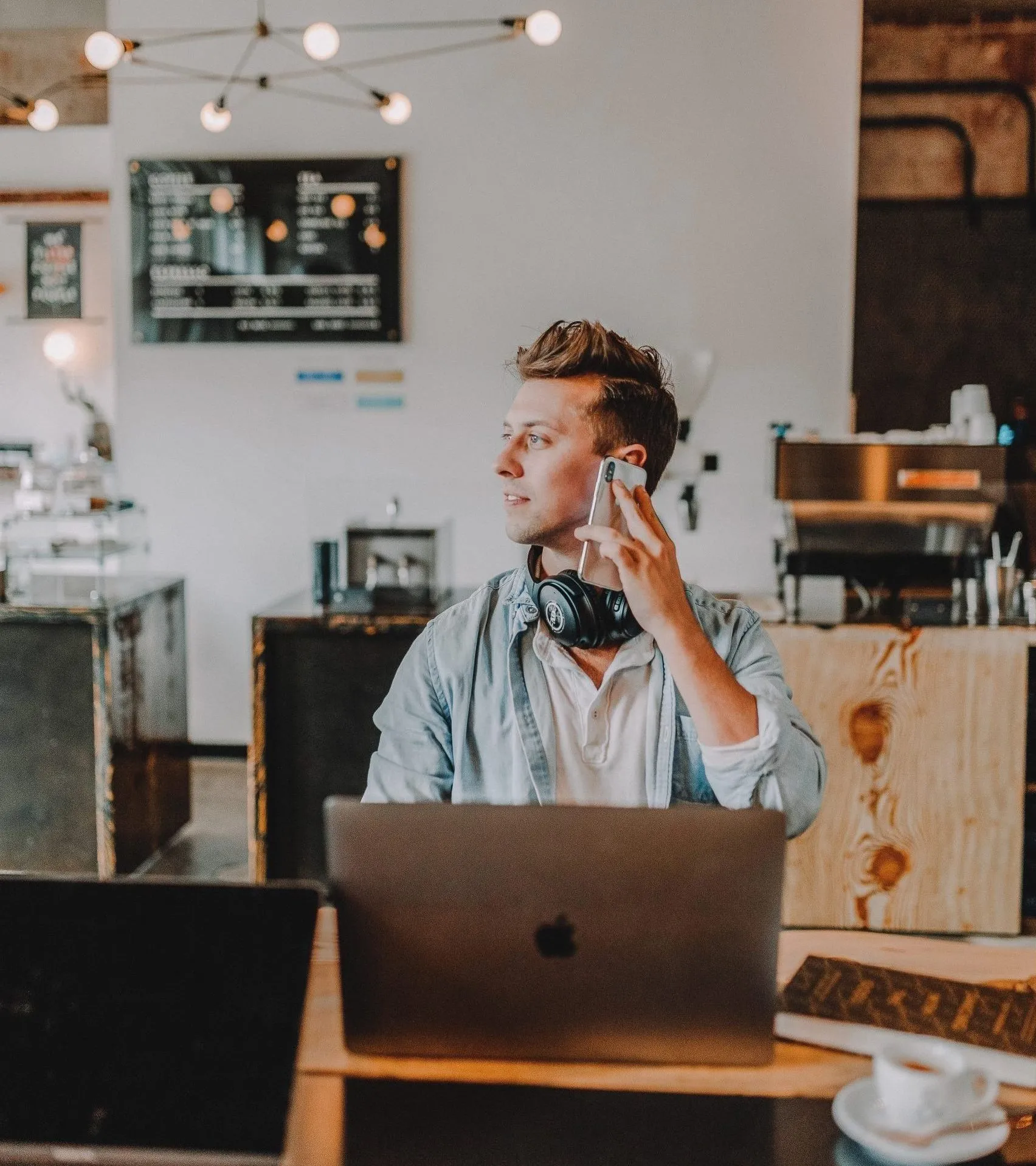 Man sitting in a cafe with his laptop while talking on his phone