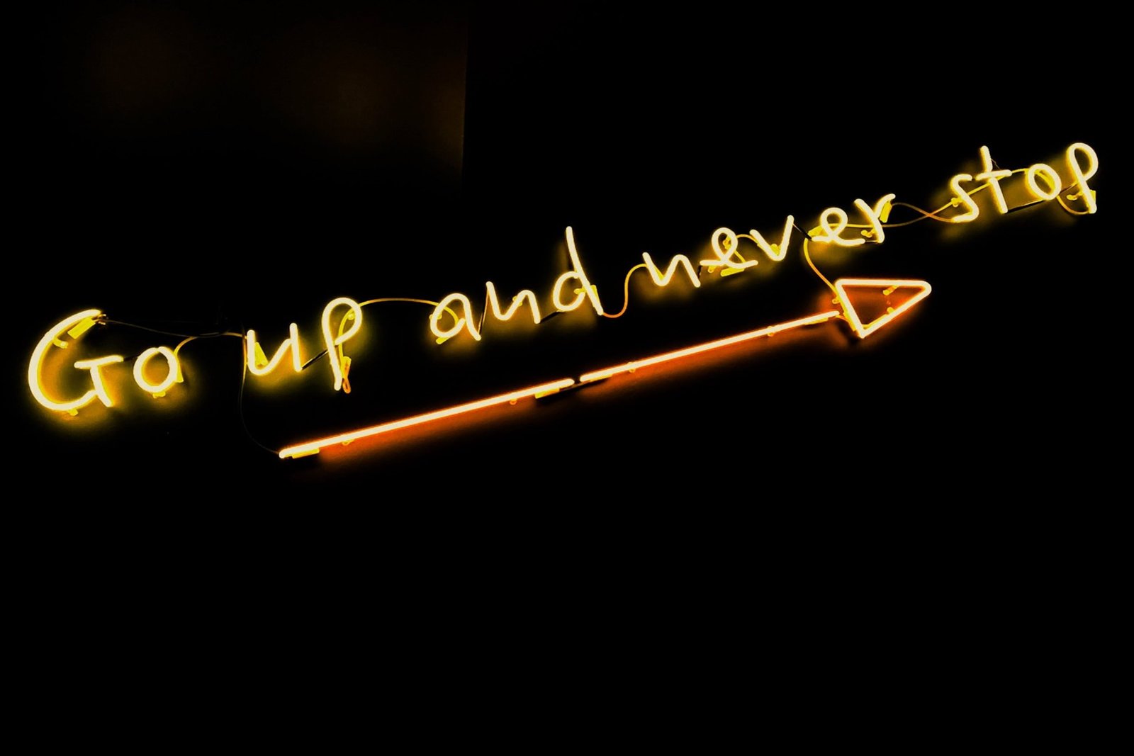 yellow neon sign saying: go up and never stop