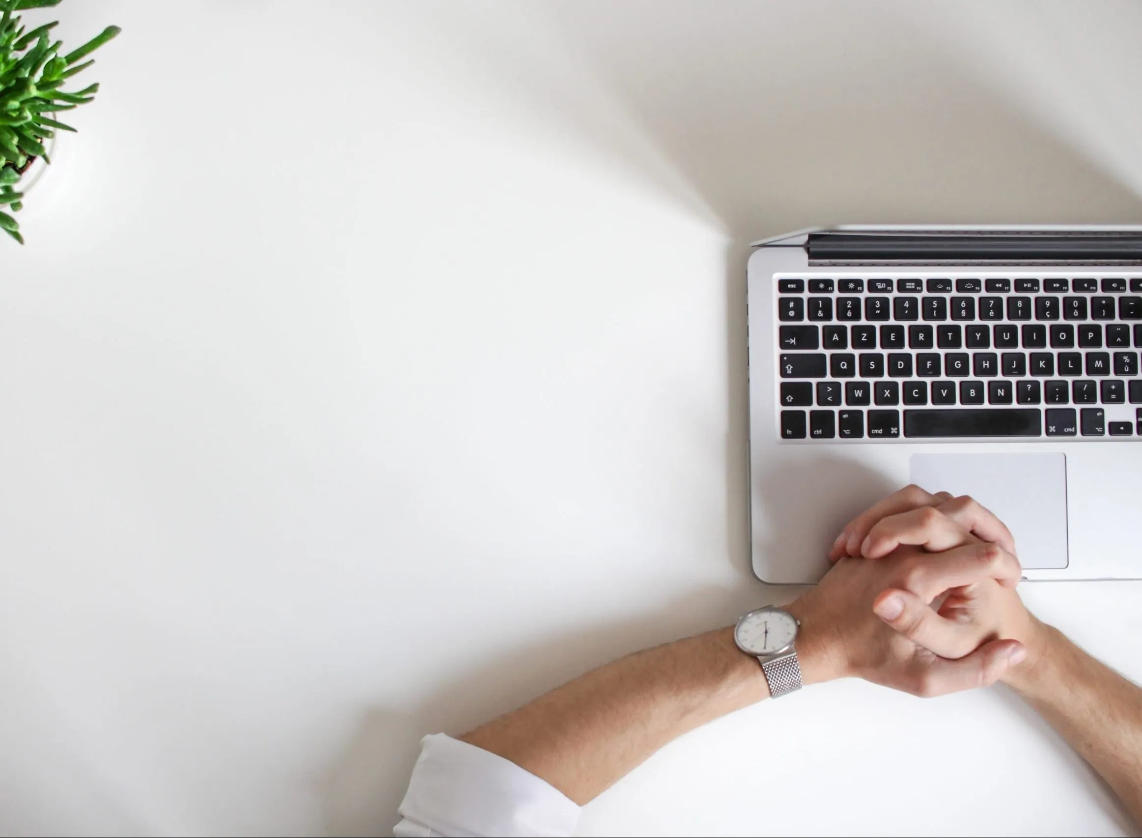 Hands folded together over a laptop on a clean desk