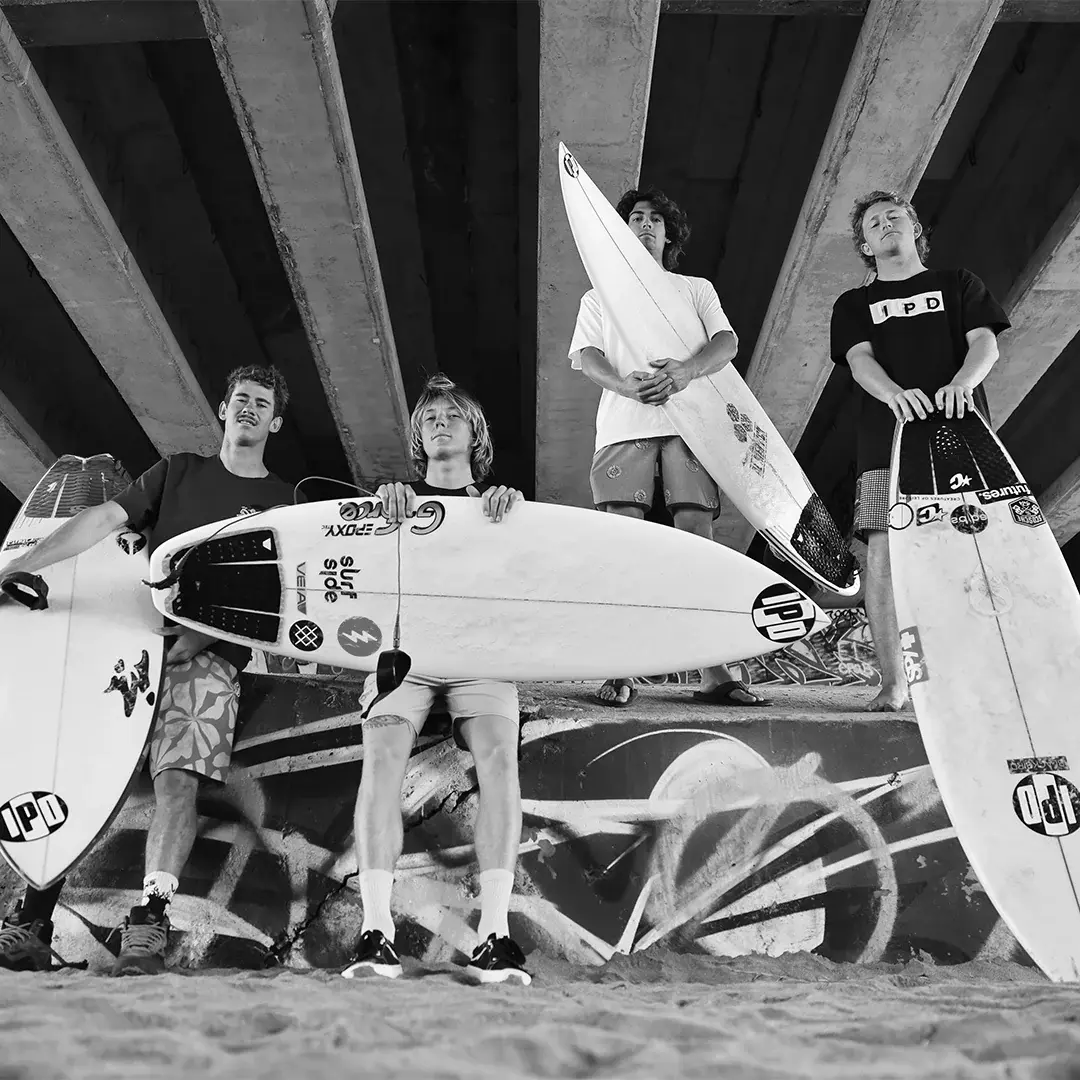 A group of young surfers pose under a bridge with their surf boards