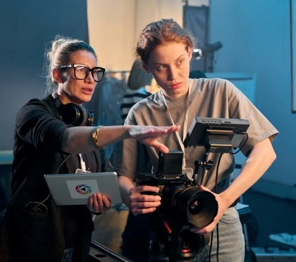 Two women on a film set, one directing, one operating a camera.
