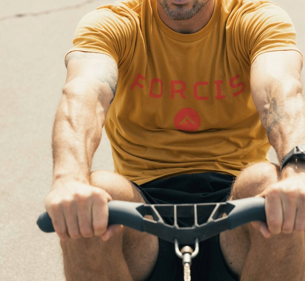 Man in a mustard Forcis logo t-shirt using an exercise machine.