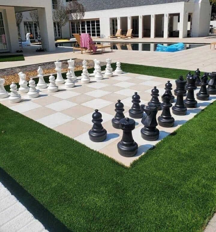 Giant outdoor chess set on a lawn beside a backyard pool.