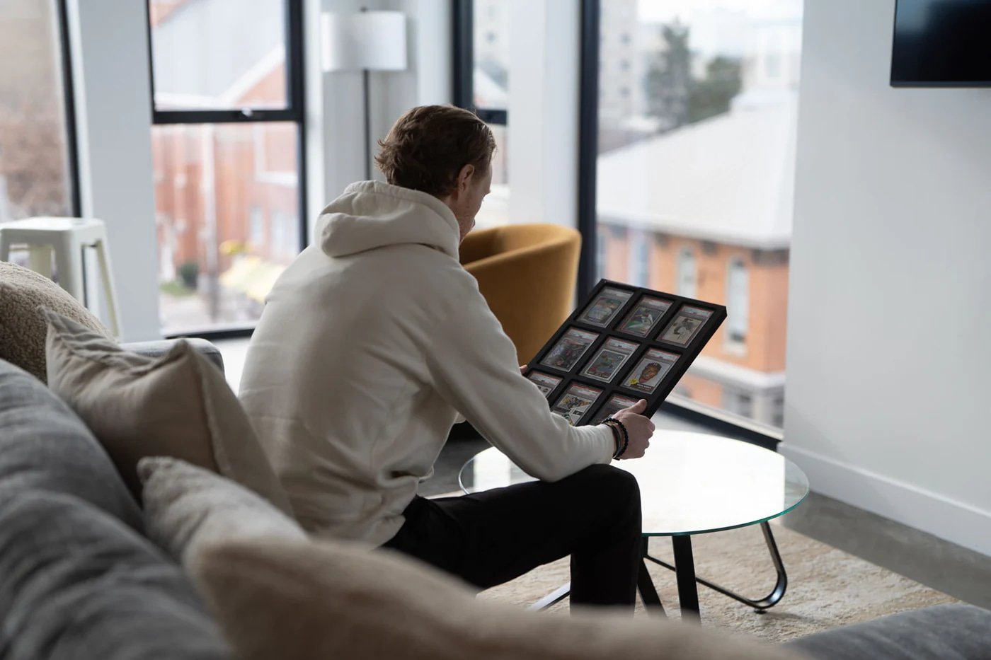 Man holding a Vaulted trading card display case in a bright living room.